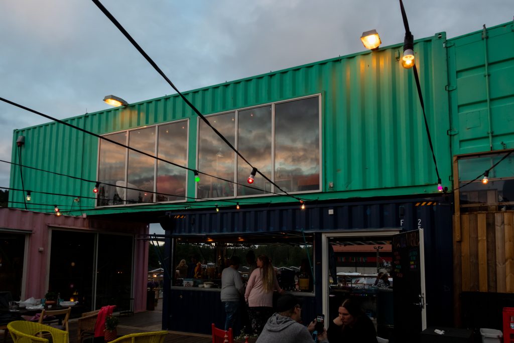 Outdoor front facade night view of a container pop-up restaurant with windows and a bar with people in Ullared Sweden.